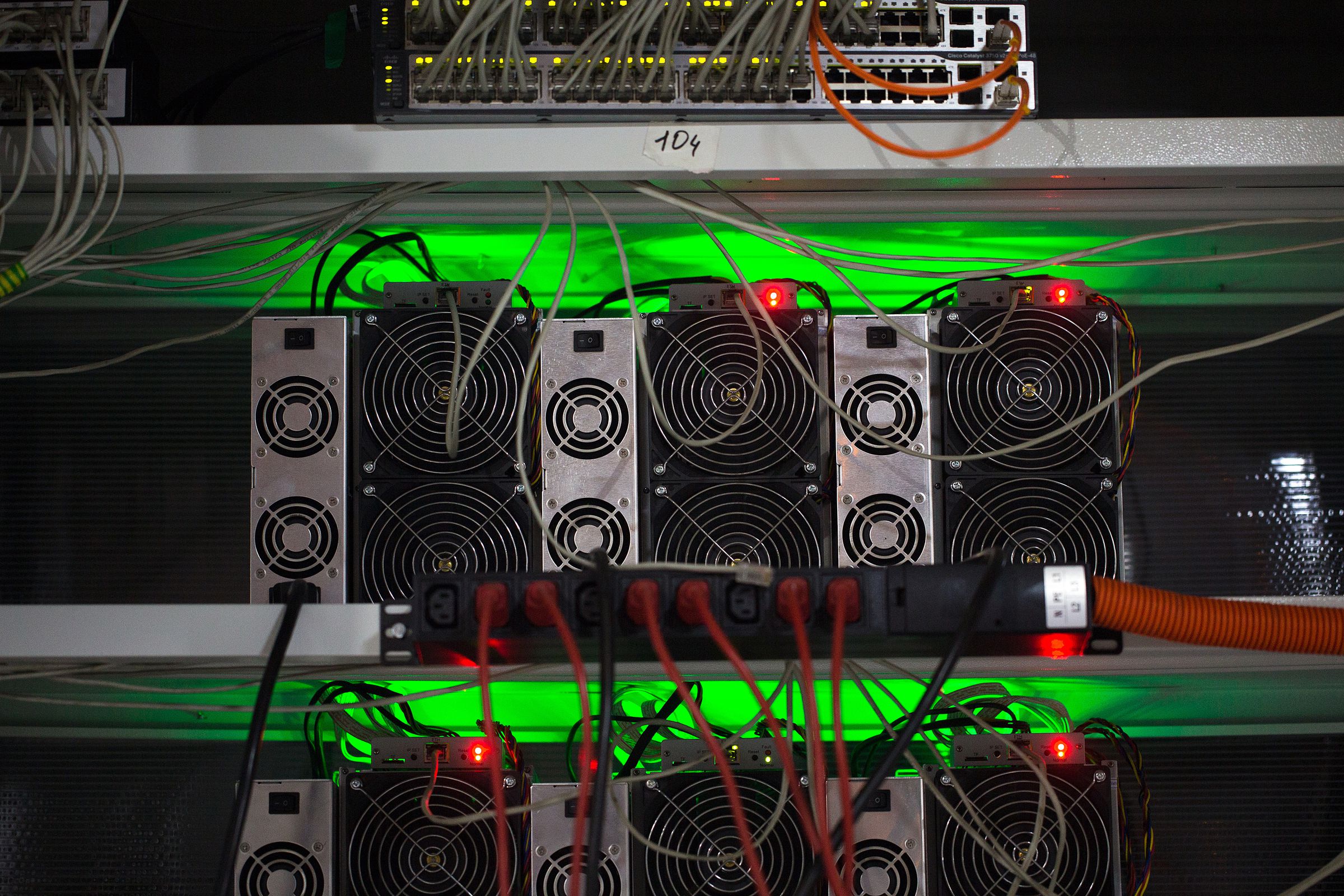 Wires stick out of specialized computers for Bitcoin mining glowing with green light