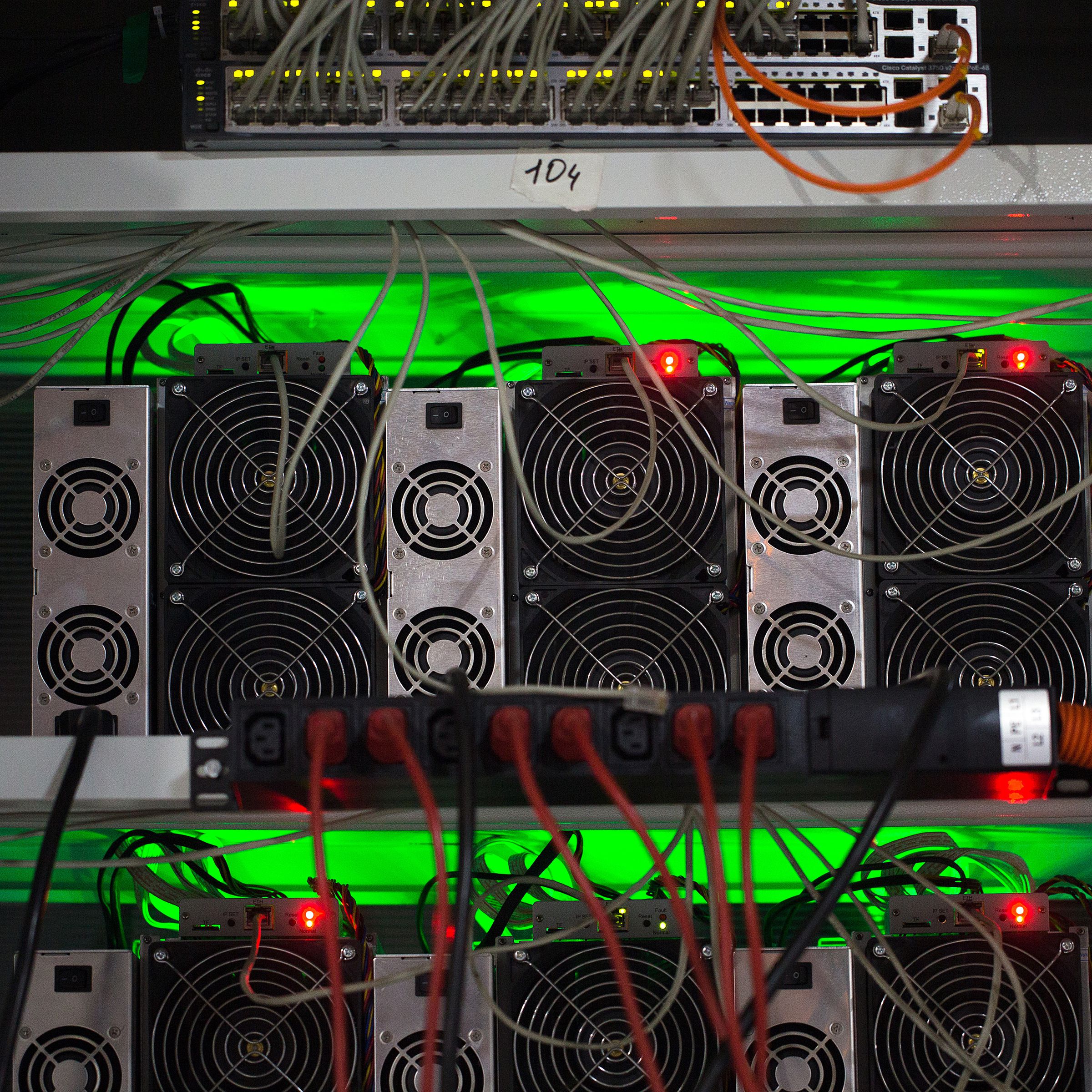 Wires stick out of specialized computers for Bitcoin mining glowing with green light