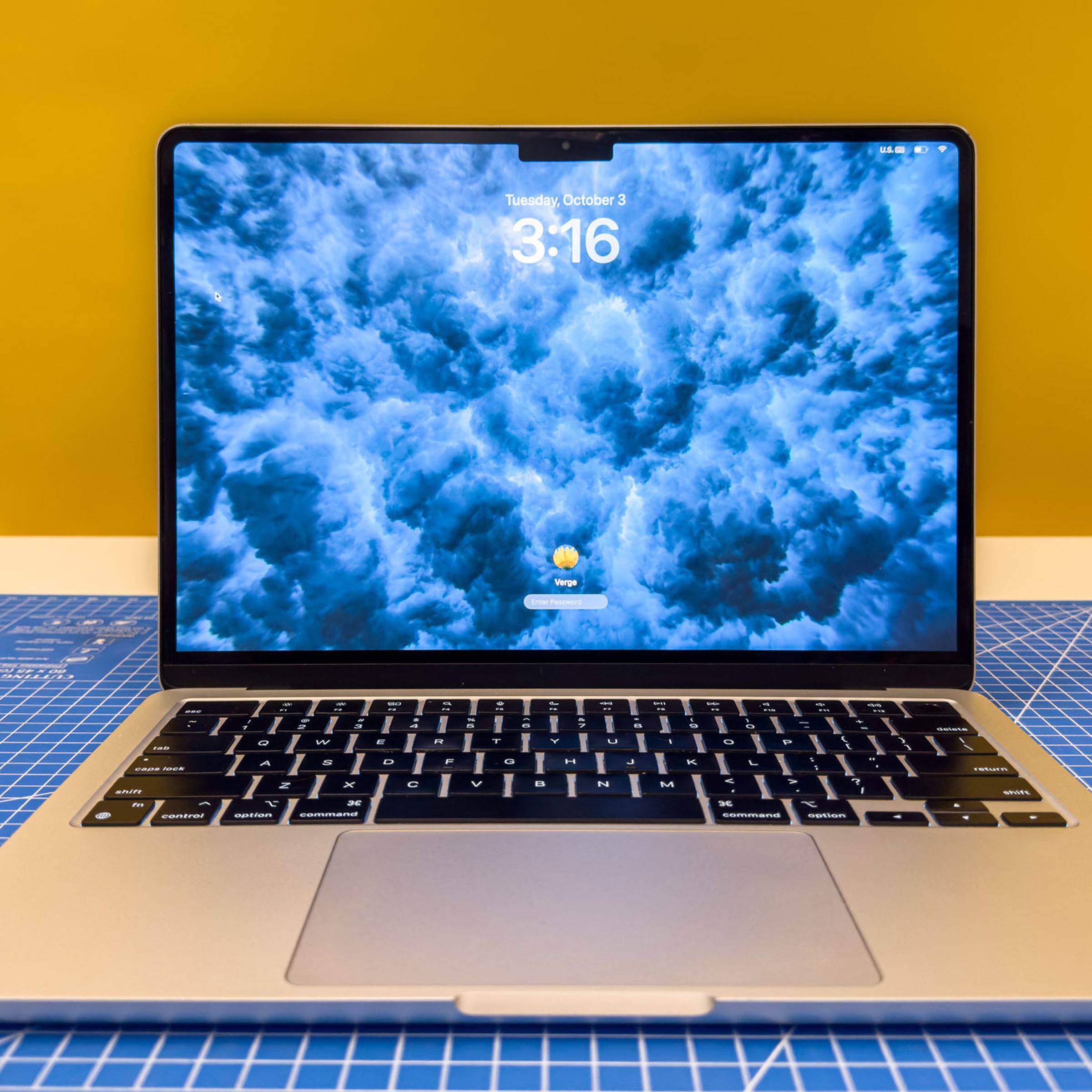 A MacBook Air displaying a macOS Sonoma dynamic wallpaper with a lockscreen overtop.