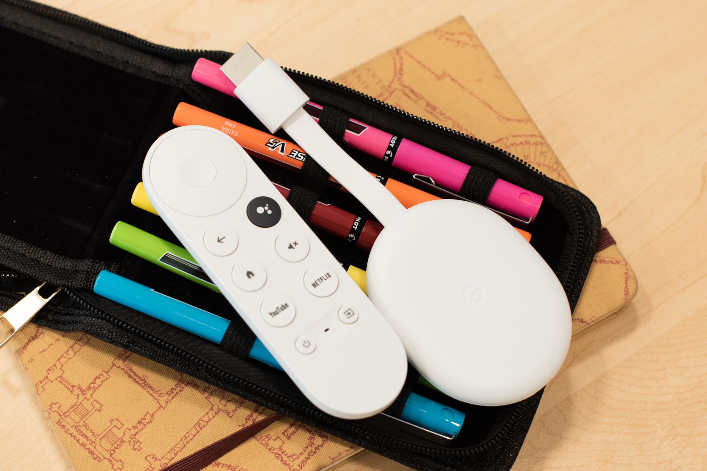 The Chromecast with Google TV (4K) with its remote lying on a pack of pens.