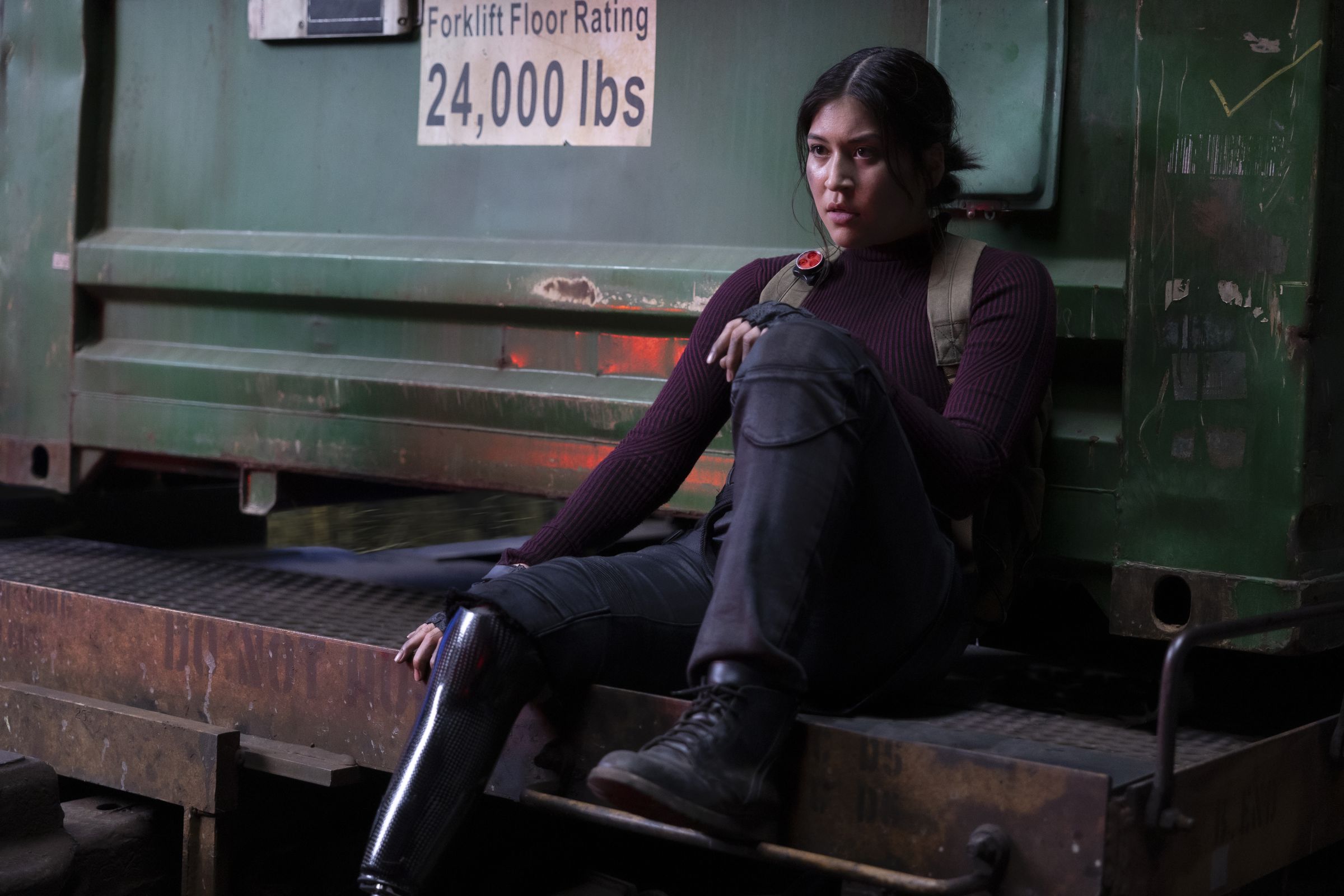 An image of Alaqua Cox as Maya Lopez. She’s dressed in combat gear and sitting on machinery looking exhausted after a fight.