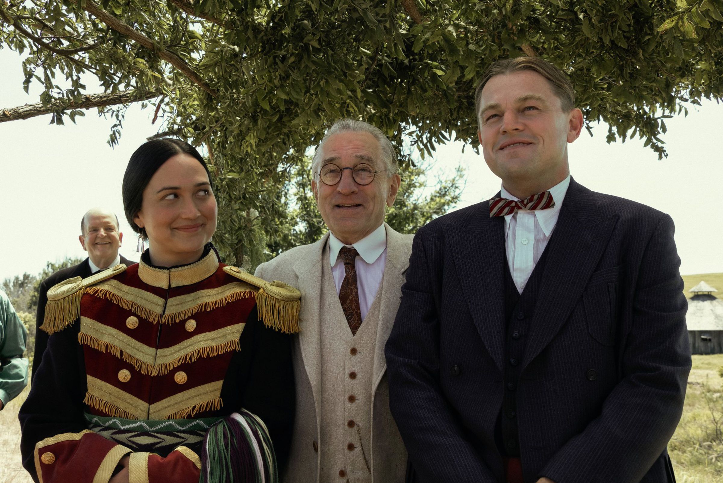 A still image from the movie showing stars Lily Gladstone, Robert De Niro and Leonardo DiCaprio standing next to each other.