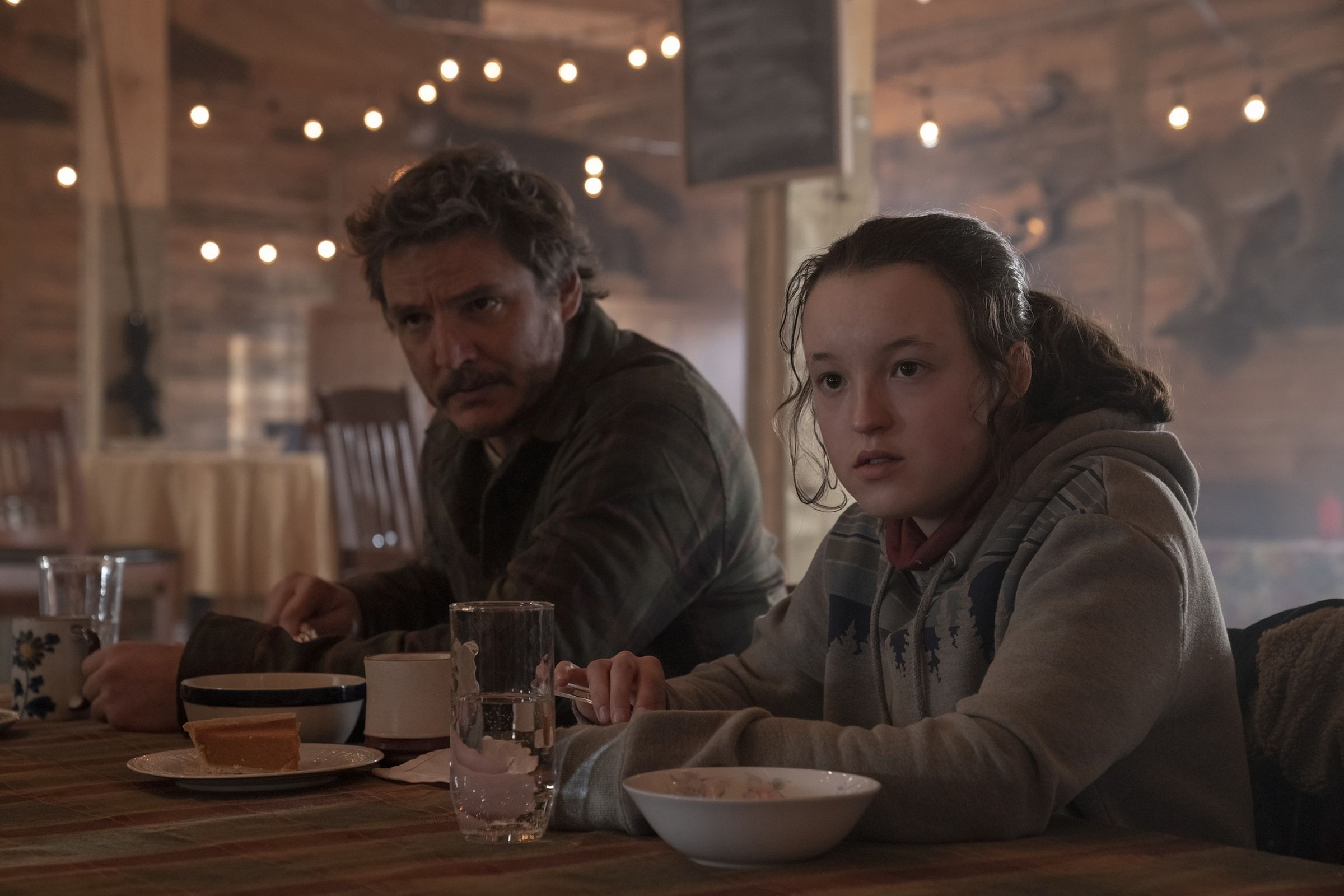 A man wearing a sweater and a girl wearing a hoodie sitting at a table eating breakfast.