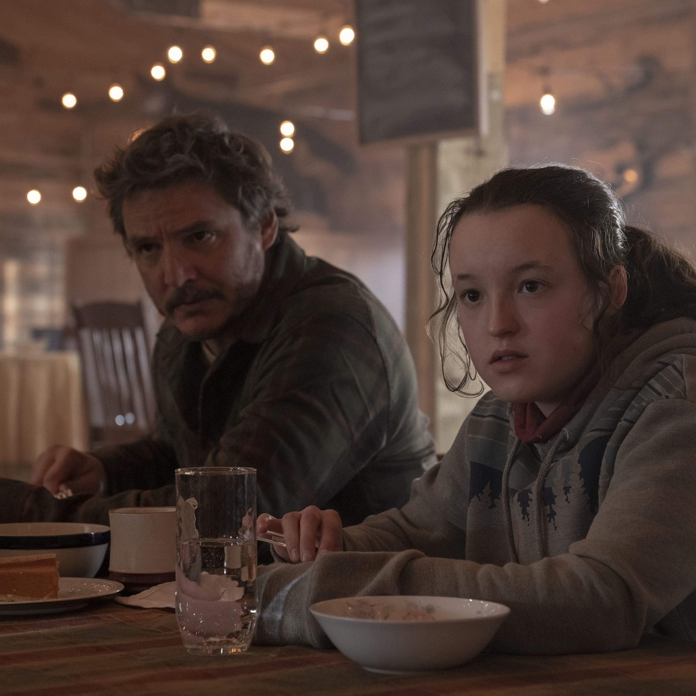 A man wearing a sweater and a girl wearing a hoodie sitting at a table eating breakfast.